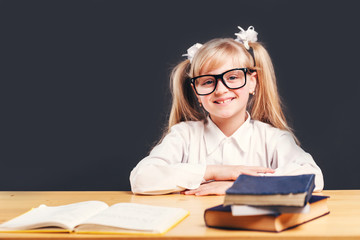 Portrait of cute young girl wears smart eyeglasses learning English language with book before dark background