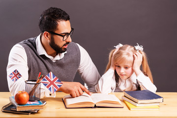 Teacher explaining new material to the primary tired student girl at the table with books