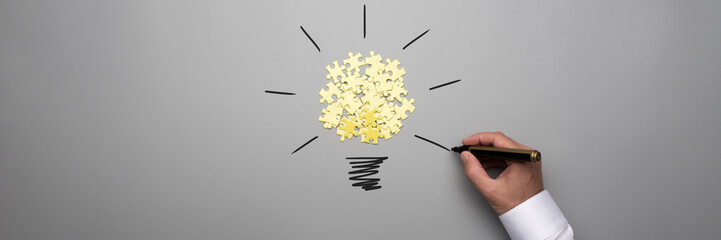Wide panorama view of puzzle pieces and male hand drawing light bulb