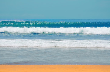 Sea sandy coast with blue water and small waves, clouds on a blue sky on a summer day.