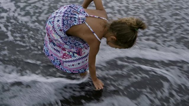 Cute little girl playing with crab, soaking it in ocean water and then showing at camera while playing on beach
