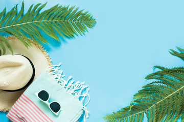Tropacal vacation. Straw beach sunhat, sun glasses, beach towel, leaf of fern on blue background....