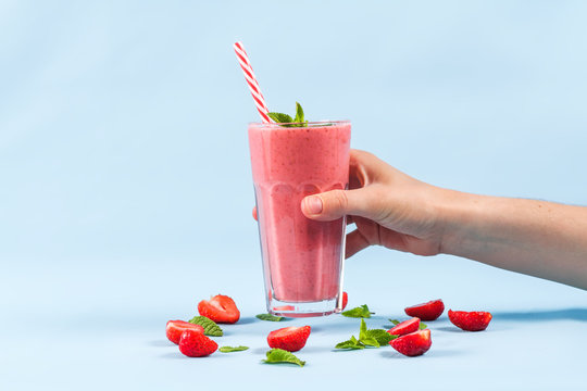A glass of strawberry smoothie with mint in hand on a blue background