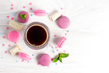 A cup of coffee, macaroons and a mint leaf on a wooden white table.