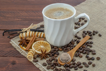 taza de cafe sobre una mesa de madera rústica decorada con granos, canela, y vainilla 