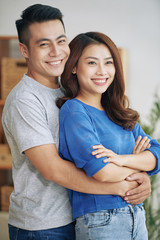 Handsome Asian man and woman embracing happily and standing together indoors looking in different sides