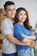 Fototapeta premium Handsome Asian man and woman embracing happily and standing together indoors looking in different sides