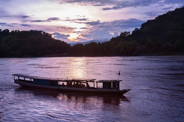 Small tour boat cruises along the Mekong river in Luang Prabang, Laos, during sunset