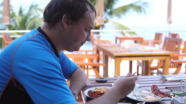 Young man eating breakfast sitting in a beach cafe. slow motion. 3840x2160