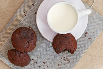 Chocolate cookies with milk on wooden desk. Tasty round biscuits. View from above. Copy space. Selective focus.