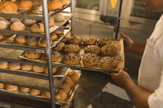 Male baker removing a tray of sweet foods in bakery