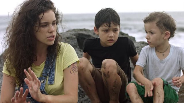 Medium shot of young curly haired woman sitting next to her two sons or brothers of elementary school age and telling something to them