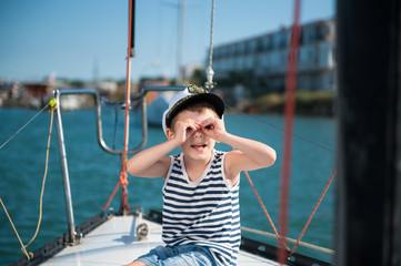 funny smiling kid in captain hat looking imitating binoculars by hands on yacht