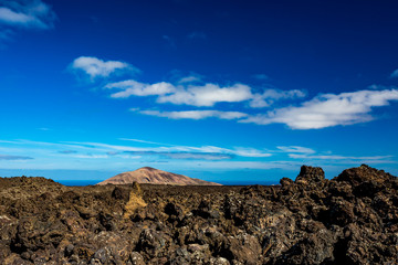 Fototapeta na wymiar The vast emptiness and loneliness of the Lanzarote black frozen lava volcanic desert and one eroded brown hill in the background