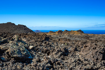 The vast emptiness and loneliness of the Lanzarote black frozen lava volcanic desert with the blue waters of the Atlantic Ocean in the background