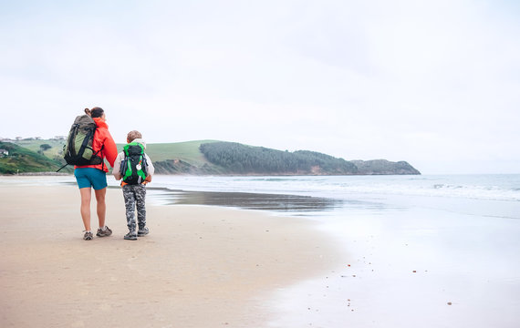 Walking travel with child. Mother and son walks together on sandy beach on the famous Camino del Norte Way, Spain