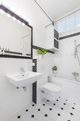 Mirror above washbasin in black and white bathroom interior with toilet and bathtub. Real photo