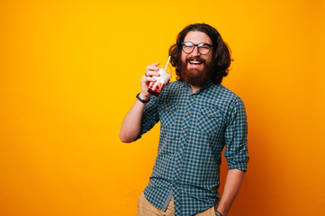 Cheerful young bearded man smiling and looking at the camera is holding his milk shake with...