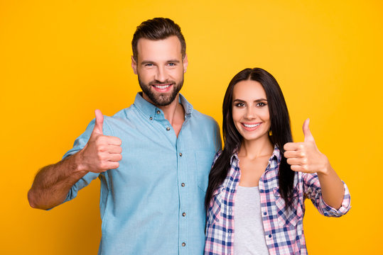 Portrait of lovely cheerful couple gesturing thumbs up with fingers looking at camera having beaming smiles isolated on vivid yellow background. Advertisement concept