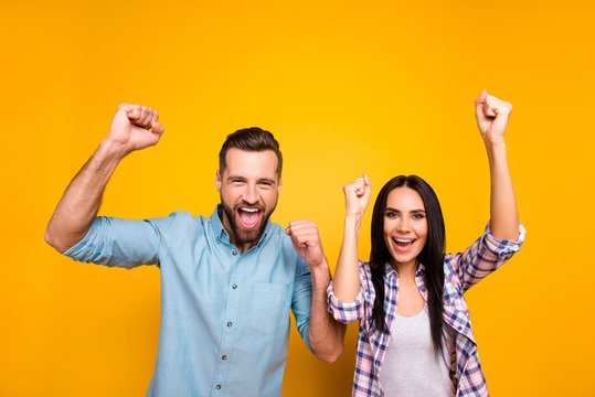 Portrait of joyful lucky couple with raised arms celebrating victory of football team yelling loudly isolated on vivid yellow background