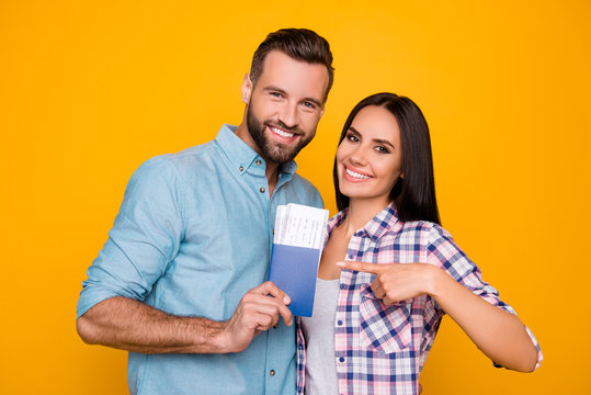 Portrait of joyful glad couple holding passport with flying tickets in hands pointing with forefinger looking at camera isolated on bright yellow background
