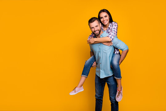 Advertisement concept. Portrait with copy space empty place of handsome man carrying on back pretty woman looking at camera isolated on vivid yellow background
