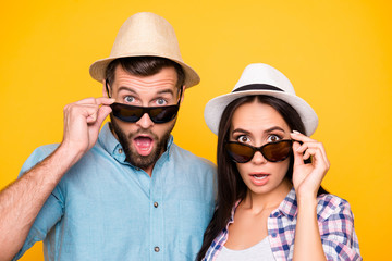 Head shot portrait of depressed shocked couple looking out black eyeglasses with wide open eyes mouth isolated on vivid yellow background