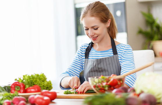 happy woman preparing vegetable salad in kitchen