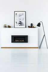 Poster above black fireplace in white minimal living room interior with lamp. Real photo