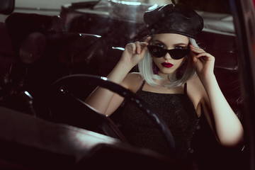 Fototapeta na wymiar beautiful fashionable blonde girl in beret and sunglasses sitting in car and looking at camera