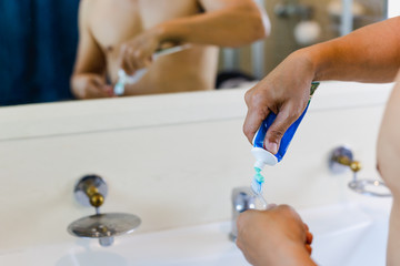 Man squeezing toothpaste into toothbrush in the bathroom