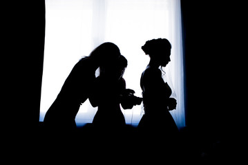 Female trying on wedding dress in a shop with two women assistants.