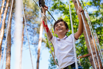 Brave kid. Happy preteen boy having fun at adventure park and smiling happily while walking down...