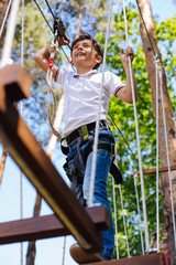 Fun experience. Charming preteen boy making steps along rope trail and having fun while smiling happily, enjoying the height
