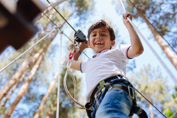 I am not afraid. Upbeat preteen boy looking down while moving along the trails at a rope part and smiling, being not afraid of height
