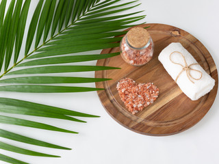 Beautiful pink Himalayan salt placed in heart shape and towel on wooden plank. Decorated by paml leaf. Relaxation and spa concept.