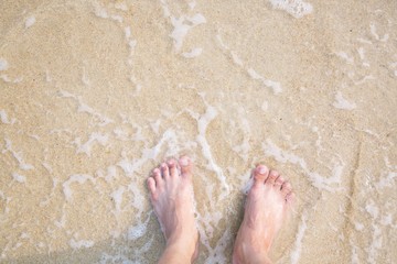 Closeup of a man's bare feet stand at wet on the beach , with a wave's edge foaming gently beneath them. Vacation on ocean beach, foot on sea sand. Leave empty copy space Enter the text above.