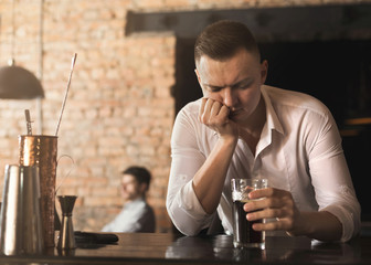 Sad young man looking at glass of beer at bar