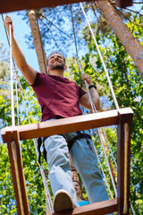 Unusual date. Cheerful young man and his girlfriend climbing at a rope park and smiling happily,...