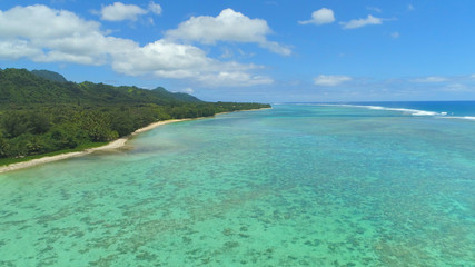 AERIAL: Turquoise ocean waves approach the white sand shore of remote island.