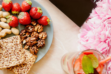 Office employee with laptop, healthy snack, water with strawberry and cucumber. Having strawberries, peanut, walnut, crispbread while working.