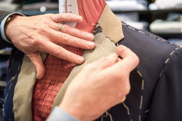 Tailor preparing bespoke suit jacket on tailors dummy, close up of hands