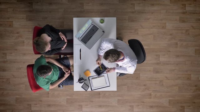 Young couple of man and pregnant woman on consultation, doctor explaining ultrasound to them, topshot, happy, medical concept