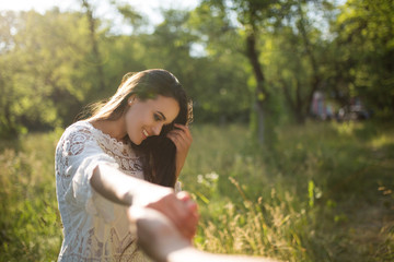 Follow me in forest in golden hour. Guy follows beautiful girl holding her hand outdoors in nature covered in soft sunlight.
