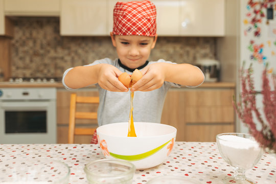 Little boy cooking. Child breaking egg into bowl. 
