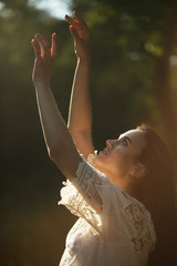 Beautiful woman lifts her hands up covered in warm sunlight. Gorgeous young girl looking up at her hands in air with soft sun rays shining on them.