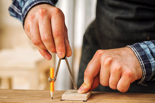 A close up of a male carpenter marks of a metal compass and a pencil on a wooden bar for making furniture.