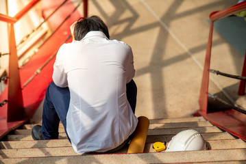 Engineer or Architect feeling stressed, worried and tired with his job while sitting on stair with...