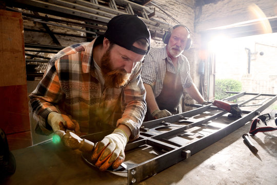 Senior blacksmith and son hammering metal on workbench in blacksmiths shop