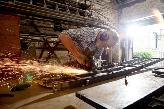Blacksmith grinding metal on workbench in blacksmiths shop - Powered by Adobe